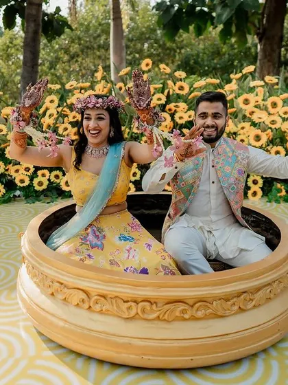 A super fun Haldi entry. This shot captures the couple's playful spirit as they pose in a giant urn, surrounded by a sea of sunflowers.