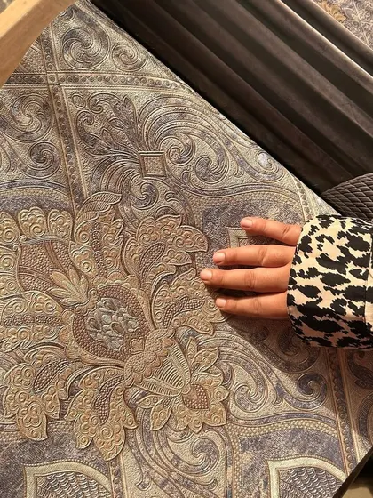 A client's hand feels the rich texture of our vintage-style wallpaper. This image captures the tactile quality of our designs, which feature classic patterns perfect for creating a warm and sophisticated atmosphere.