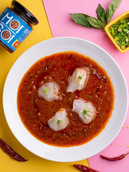 Jhol momos swimming in a spicy, flavorful sauce. The bright, dual-toned background makes this popular street food dish look modern and exciting, perfect for a trendy food brand.