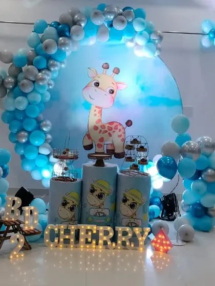 A cute and gentle animal theme featuring a friendly giraffe. This setup for Cherry's 2nd birthday uses a blue and silver color palette, a circular backdrop, and light-up marquee letters for the name.