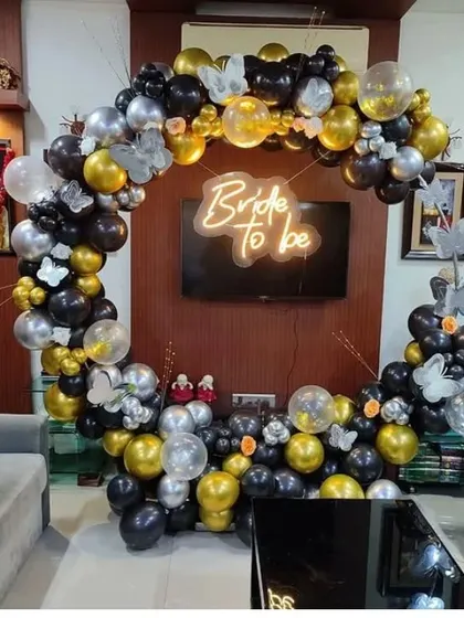 Another view of the black, gold, and silver balloon arch, showing how it can frame a TV or wall unit. The butterfly accents add a touch of delicate detail to the bold color scheme.