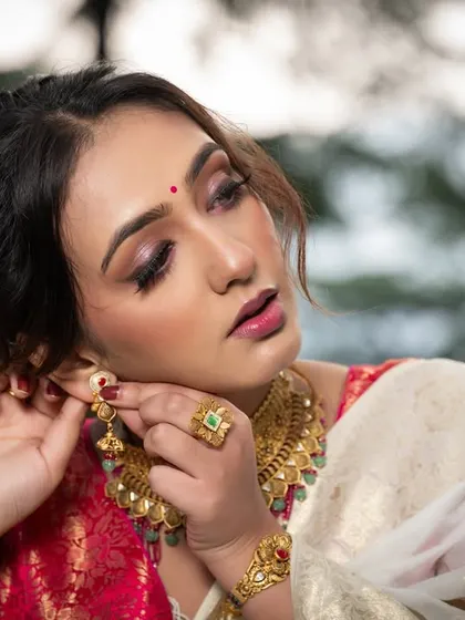 The model adjusting her earring, a classic pose that draws attention to the beautiful gold jewelry.
