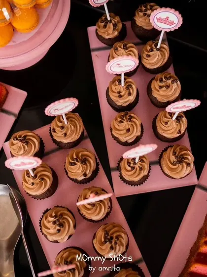 A top-down view of a princess-themed dessert table, featuring chocolate cupcakes with custom crown toppers and other pink-hued treats. I ensure even the food matches the magical theme.