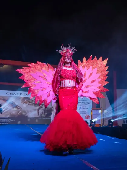 A model in a striking red mermaid gown with large, fiery wings, making a dramatic statement on the runway.