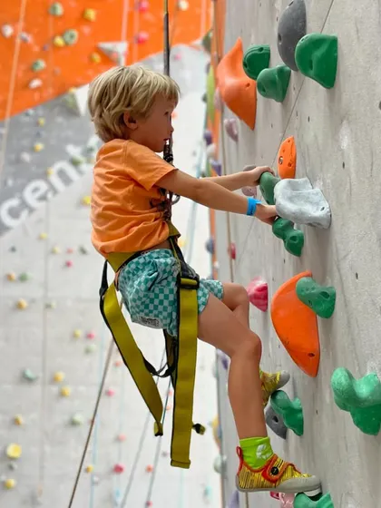 A young boy hangs from the auto belay rope, enjoying the ride down after reaching the top. The descent is just as much fun as the climb!