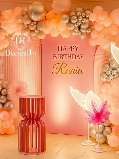 A dreamy and modern first birthday setup for Rania. The design features a glowing balloon arch in peach and silver, with illuminated butterfly and flower props for a touch of whimsical elegance.