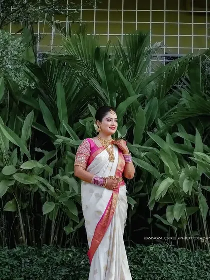 The bride stands against a vibrant green wall of plants, making the pink border of her white saree pop. This is a fresh and modern take on a traditional bridal portrait.