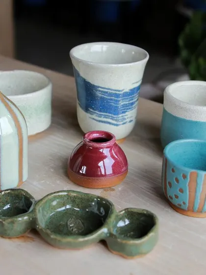 A colorful group of cups, bowls, and a small pitcher, showcasing various glazing techniques like stripes and dipping.
