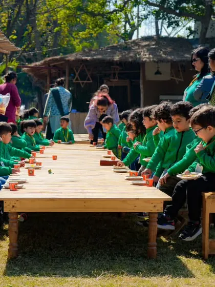 A class of students sitting at a long wooden table, engaged in a painting or craft activity.