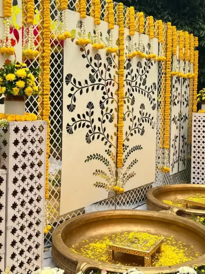 A modern twist on a classic Haldi, this setup features elegant mirror panels with floral motifs, traditional brass 'urlis', and strings of marigolds for a look that is both timeless and contemporary.