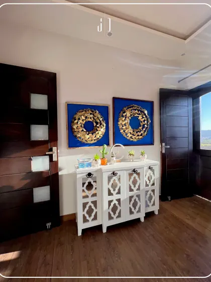 A beautifully designed entryway featuring a white console table with intricate lattice work, flanked by dark wooden doors. The bold blue and gold wall art adds a striking pop of color and serves as a focal point.