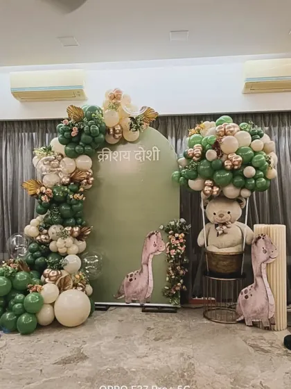A cute dinosaur-themed decoration in sage green and beige. This setup includes dinosaur cutouts and a teddy bear in a hot air balloon basket, blending adventure with classic baby shower elements.