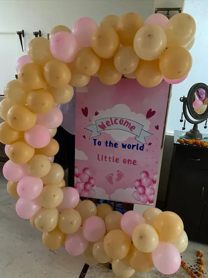 A sweet 'Welcome to the world little one' sign on an easel, framed by a semi-arch of pastel pink and peach balloons for a baby's homecoming.