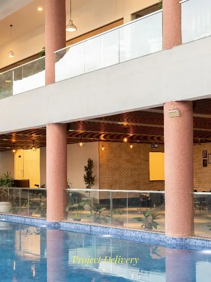 The poolside at the Sona Vistaas Clubhouse, framed by terracotta-colored columns. The design connects indoor and outdoor leisure areas, with the upper-level balcony overlooking the pool to foster a sense of community and shared experience.