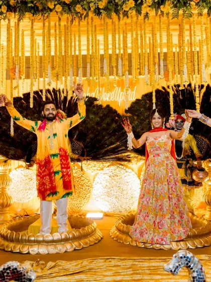 The couple celebrating on stage during their Haldi, surrounded by stunning yellow floral decor.