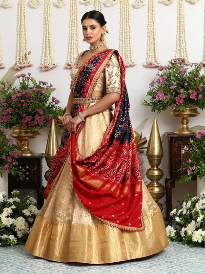 A truly regal look, this gold silk lehenga is paired with an embroidered blouse and a stunning red and navy Bandhani dupatta, draped elegantly.