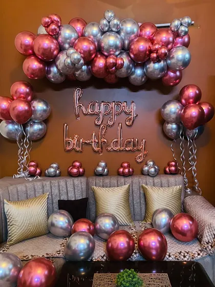 A simple yet chic living room decoration. This setup uses chrome balloons in rose gold and silver, arranged over a sofa with "happy birthday" foil letters.