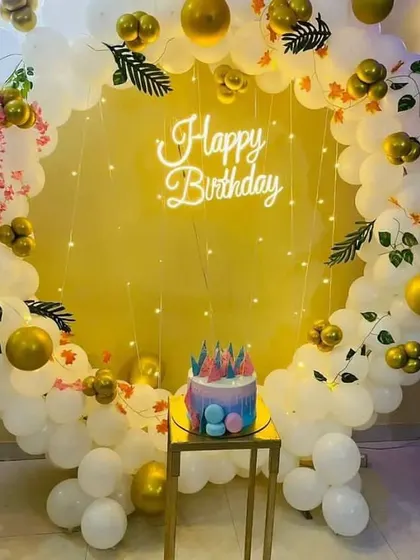 An elegant and classic birthday backdrop with a full ring of white and gold balloons, decorated with small leaves and fairy lights for a sophisticated look.