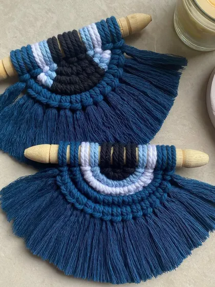 Protect your space with our mini macrame evil eye wall hanging. This piece features shades of blue, black, and white, intricately knotted to form the protective symbol.