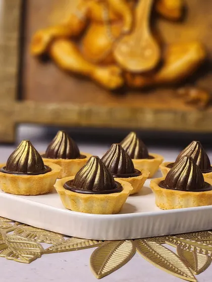 A close-up of the handcrafted chocolate modak tarts. The buttery tart shell is filled with a rich chocolate ganache, shaped into a perfect modak.