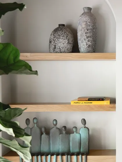 An arched wall niche frames a collection of curated artifacts, including textured vases and a bronze sculpture of human figures. This is how we create personal, gallery-like moments within a home.