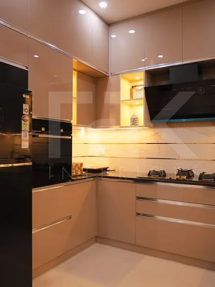 A modern kitchen with glossy beige cabinets, a black countertop, and integrated appliances. The warm under-cabinet lighting highlights the workspace and adds to the sophisticated feel.