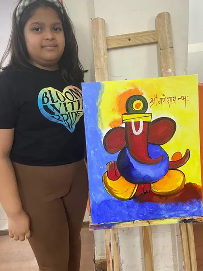 A student proudly stands by her vibrant, modern Ganesha painting on an easel. Our classes encourage students to explore different artistic styles, from traditional to contemporary.
