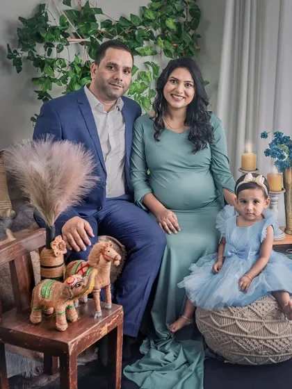 A beautiful family portrait from a maternity session, with the expecting mother, her husband, and their young daughter. The warm, earthy tones of the boho studio setup create a cozy and inviting feel.