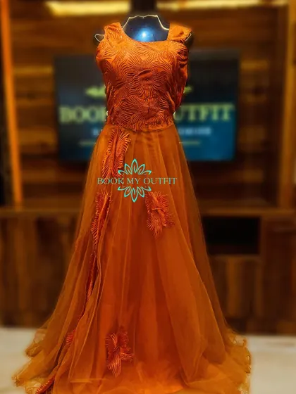 This burnt orange gown features a textured bodice and delicate floral appliques cascading down the skirt. The A-line silhouette and tulle fabric give it a soft, romantic feel.