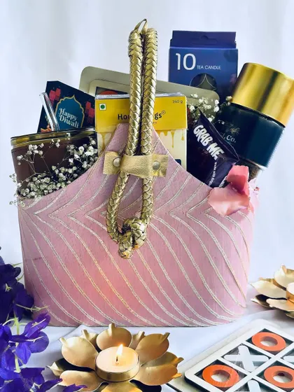 This luxurious Diwali hamper, presented in a pink fabric basket with a golden handle, includes a fun XOXO game, a coffee tumbler, scented candles, and gourmet treats for a complete festive package.
