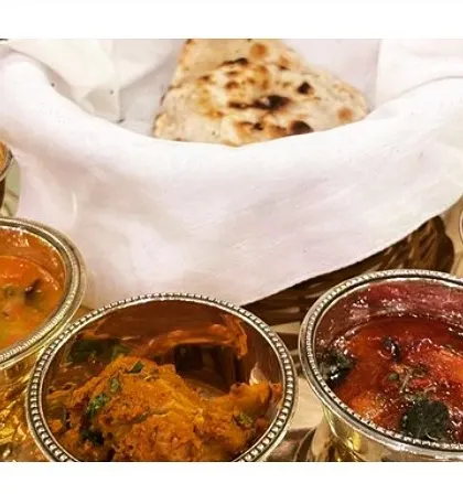 A mini thali presentation, offering a taste of multiple curries in elegant silver bowls, served with freshly baked naan. This is perfect for a formal, seated dinner.