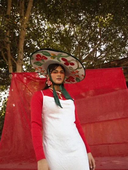 A shot from the 'LUNA' editorial, defined by its striking red and white color palette. The styling features a large, hand-painted sombrero-style hat, which acts as a central artistic element against the dramatic red fabric backdrop.