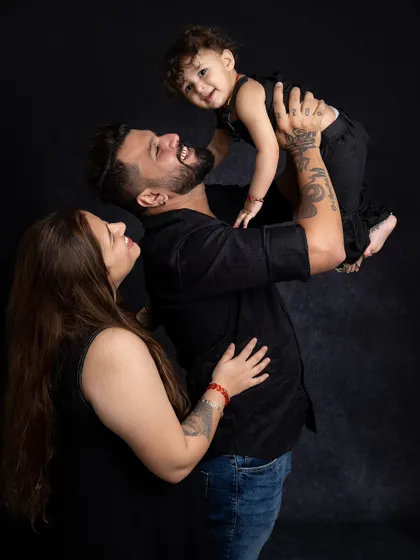 A beautiful family portrait against a dark backdrop. The parents are looking lovingly at their child, creating a powerful and emotional image.