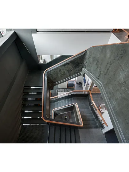 The main staircase railing is a single, sweeping curve made of ferrocement with a wooden handrail. This sculptural element creates visual interest and guides visitors physically and visually through the multi-level space.