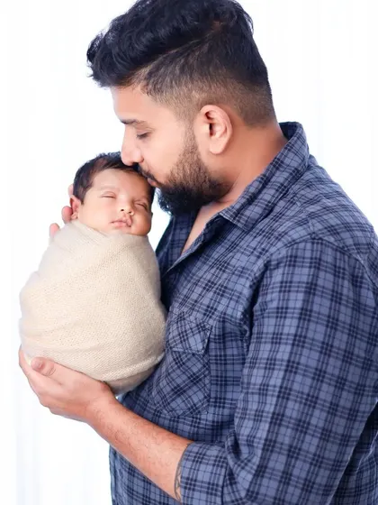 A father in a casual setting holding his swaddled baby. We ensure dads are comfortable and included in the newborn photoshoot.