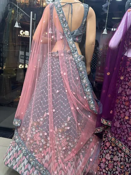 A back view of a grey lehenga with pink and blue floral embroidery on a mannequin, showing the intricate details and back design of the blouse.