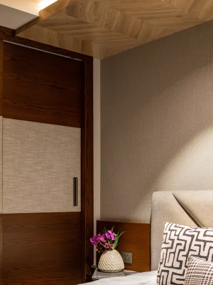 A detail of the master bedroom, showing the custom wardrobe with fabric paneling next to the geometric headboard and herringbone ceiling. The layering of textures creates a rich, tactile experience.