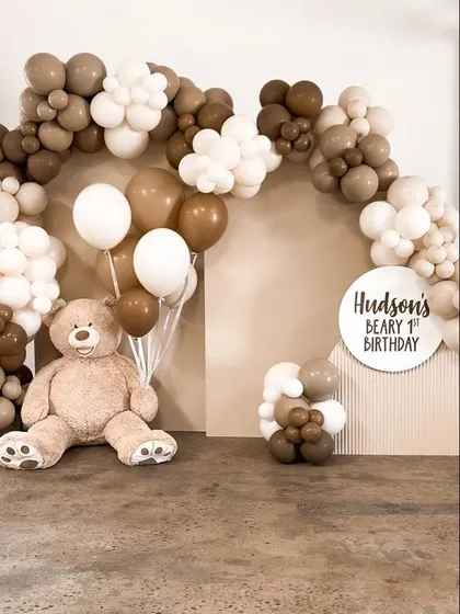 A minimalist and modern teddy bear first birthday theme. This "Hudson's Beary 1st Birthday" setup uses a neutral palette of brown and white balloons with a large teddy bear.