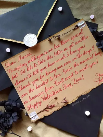 A beautiful note for Valentine's Day, written in a flowing red script on kraft paper. The piece is accented with washi tape, a dried flower, and a custom wax seal on a black envelope.