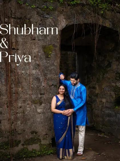 An elegant pre-wedding portrait of a couple against the weathered stone wall of a fort, their traditional blue outfits creating a striking visual.