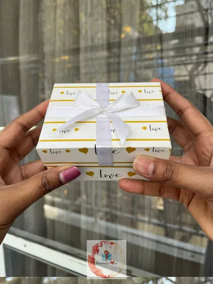 A beautifully wrapped small gift box with a "love" and hearts pattern, tied with a simple white ribbon.