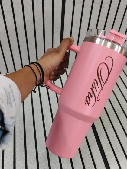A light pink travel tumbler with a handle, personalized with the name "Tisha". These mugs are designed to fit perfectly in a car's cup holder.