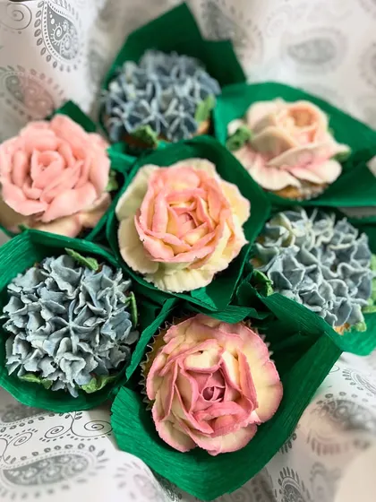 A beautiful cupcake bouquet featuring delicate pink roses and dusty blue hydrangeas, all piped from buttercream. You can customize the flowers, colors, and flavors for any occasion.