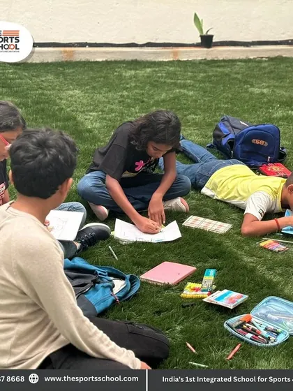 A group of students spread out on the grass, enjoying a collaborative and creative outdoor class.