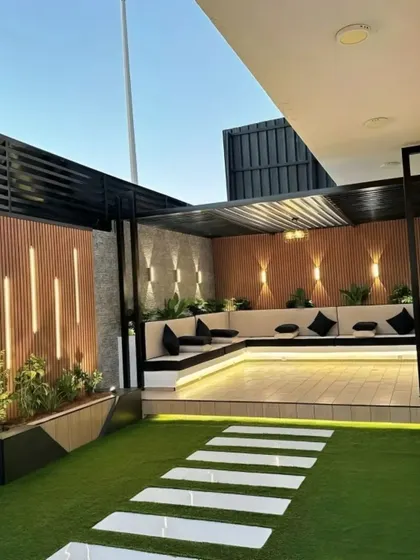 A modern backyard patio with a built-in L-shaped sofa and a sleek pergola. The integrated lighting on the wooden accent wall creates a warm and inviting ambiance for evening gatherings.