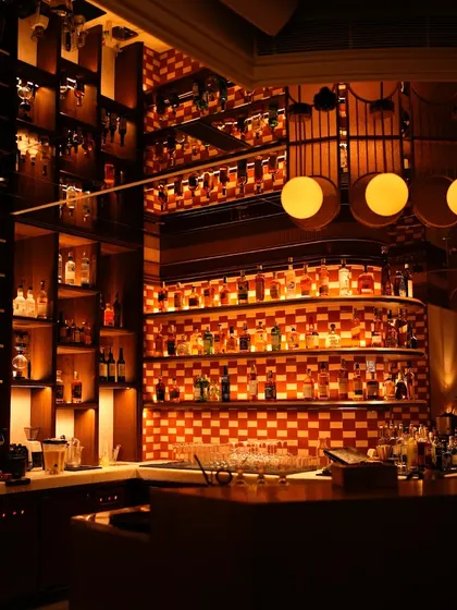 Our bar is a library of spirits. The checkered tile backsplash and warm lighting create a dramatic and inviting backdrop for our extensive collection.
