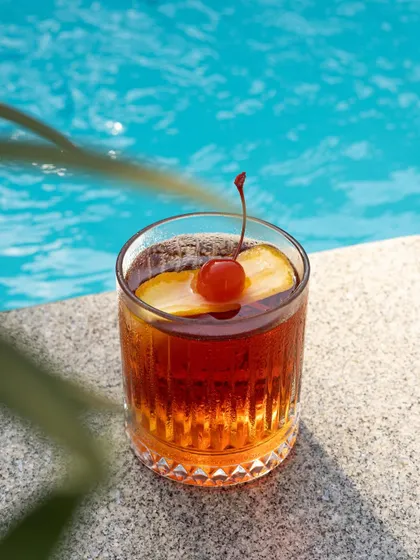 A classic Old Fashioned cocktail by the pool, with the bright blue water creating a refreshing and high-contrast backdrop.