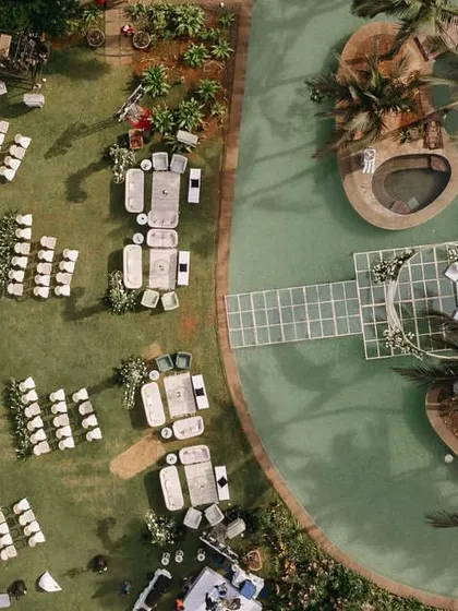 An aerial drone shot of the entire waterside wedding venue, showing the meticulous layout of the guest seating, lounge areas, and the stunning mandap on the pool.