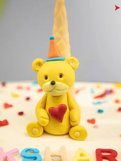 A detailed shot of the cute yellow teddy bear topper with a heart on its chest.