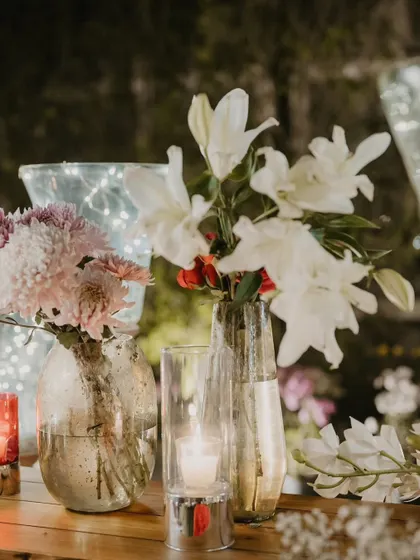 A close-up of a table centerpiece with white lilies and pink chrysanthemums, lit by a candle.
